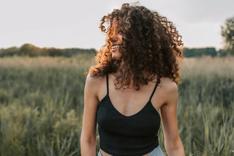 Woman with healthy curly brown hair smiling in a field